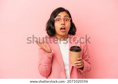 Young latin woman holding take away coffee isolated on pink background surprised and shocked.