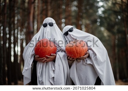A cute couple of ghosts in love are holding pumpkins in their hands. Love story. Walk in the woods. Halloween symbols.