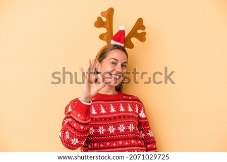 Young caucasian woman wearing a christmas reindeer hat isolated on yellow background cheerful and confident showing ok gesture.