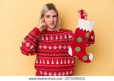 Young caucasian woman holding a elf sock isolated on yellow background showing a disappointment gesture with forefinger.