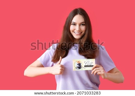 Young woman with gift certificate for massage showing thumb-up on color background