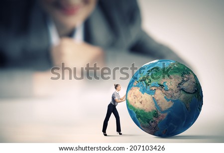 Businesswoman looking at miniature of woman rolling Earth planet. Elements of this image are furnished by NASA