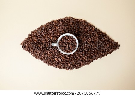 Brown eye made of caffee beans. Light Brown background. Eye cup of coffee.