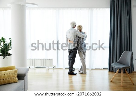 Portrait of a lonely  senior couple embracing hugging and looking through window at home Royalty-Free Stock Photo #2071062032