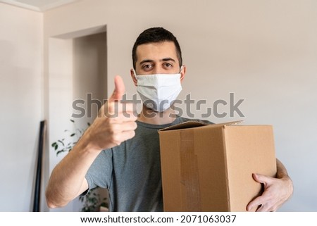 Man with face mask holding a box and waving a hand sign of approval