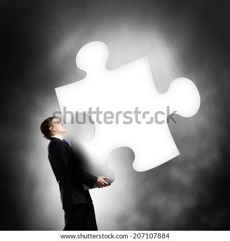 Young businessman carrying huge piece of puzzle