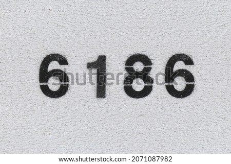 Black Number 6186 on the white wall. Spray paint. Number six thousand one hundred and eighty six.