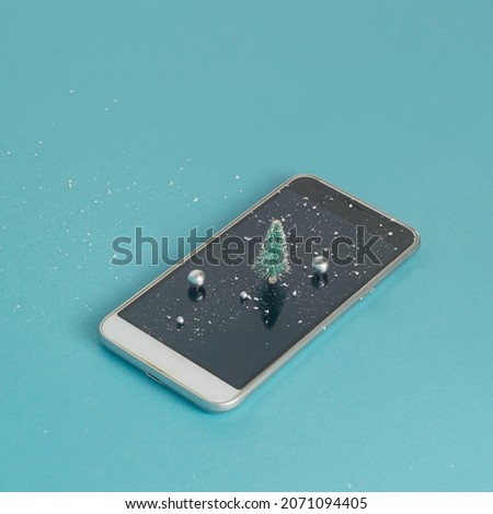 Cell Phone with Christmas tree, snow and shine balls on blue background.