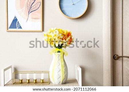 Vase with beautiful narcissus flowers and candles on table in room