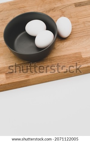 organic white eggs in a dark gray bowl and wooden chopping board on a white surface with copy space for text
