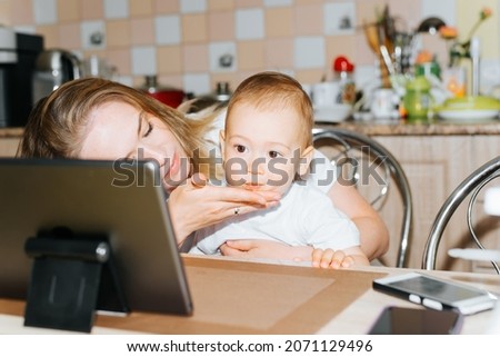 Motherhood, parenting, childcare concept. Mom and child using tablet together, watching educational children's video cartoons. Mother wiping her little son's chin while sitting in kitchen at home.