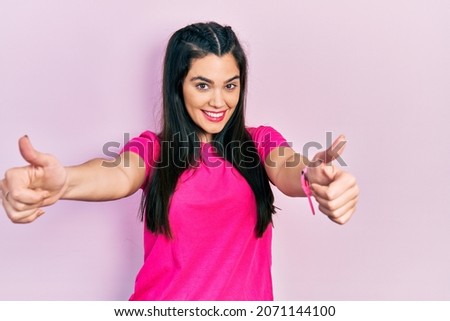 Young hispanic girl wearing casual pink t shirt approving doing positive gesture with hand, thumbs up smiling and happy for success. winner gesture. 