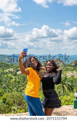 two black girls taking selfies with a phone in front of a beautiful natural landscape