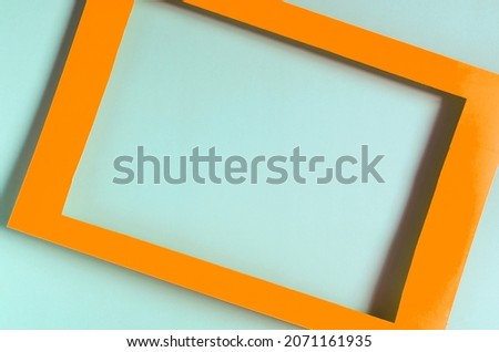 Orange paper frame on a colored background. Flat bright orange frame on a light green background close-up