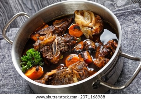 beef broth of beef meat on bones slow cooked with charred vegetables: carrot, onion, garlic, and spices served in a pot, close-up