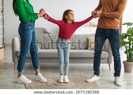 Divorce Concept. Angry parents fighting over their child, mad man and woman quarrelling, pulling daughter's hands in different directions standing in living room. Domestic Violence, Separation Royalty-Free Stock Photo #2071180388
