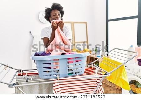 Young african american woman smelling clothes doing laundry at laundry Royalty-Free Stock Photo #2071183520