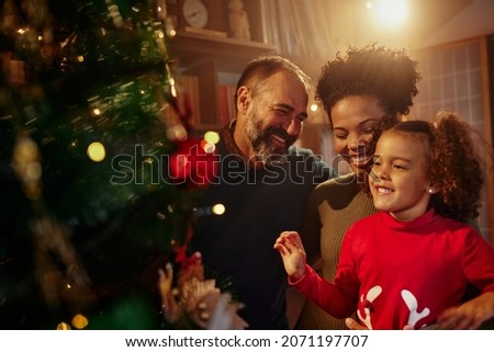 Beautiful young mixed race family enjoying their holiday time together, decorating Christmas tree, arranging the christmas lights and having fun