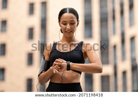 Sporty Young Woman Looking At Smartwatch On Her Wrist, Tracking Fitness Activity During Training Outdoors, Happy Fit Lady Using Modern Gadget For Checking Heart Rate Or Choosing Music For Jogging Royalty-Free Stock Photo #2071198418