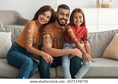 Coronavirus Vaccination Advert. Happy Vaccinated Family Of Three People Showing Arm With Sticking Plaster After Covid-19 Vaccine Vax Injection Posing Sitting On Couch In Living Room, Smiling To Camera Royalty-Free Stock Photo #2071198730