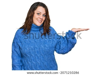 Young plus size woman wearing casual clothes smiling cheerful presenting and pointing with palm of hand looking at the camera. 