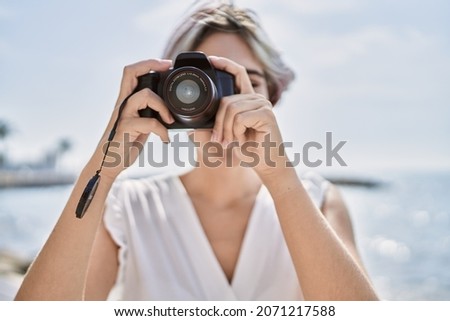 Young caucasian girl smiling happy using professional camera at the beach.