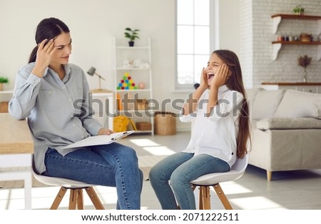 Spoilt disobedient bad tempered child throwing tantrum at appointment meeting with psychologist. Misbehaving defiant kid with anger issues covers ears with hands and won't talk or listen to therapist Royalty-Free Stock Photo #2071222511