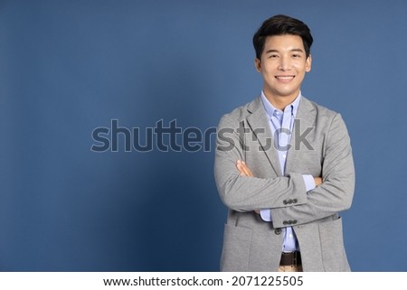 Smiling young Asian businessman with arms crossed in blue studio isolated background Royalty-Free Stock Photo #2071225505