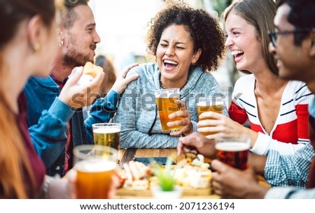 Multiracial friends drinking beer at brewery pub garden - Genuine friendship life style concept with guys and girls enjoying happy hour food together at open air bar dehor - Warm vivid filter Royalty-Free Stock Photo #2071236194