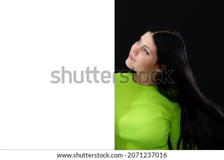 attractive dark-haired woman in bright colored clothes with a white blank poster, isolated on a dark background