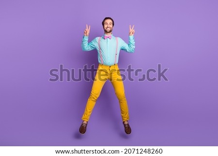 Full size photo of cute young guy jump show v-sign wear tie suspenders shirt pants sneakers isolated on purple background