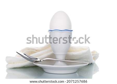 One white chicken egg with ceramic stand and spoon, close-up, isolated on white.