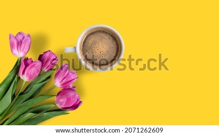 A cup of hot, morning coffee and a bouquet of tulips on a desk.