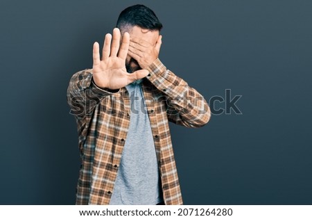 Hispanic man with beard wearing casual shirt covering eyes with hands and doing stop gesture with sad and fear expression. embarrassed and negative concept. 