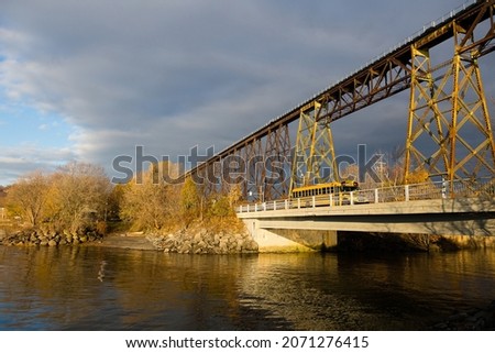 School bus crossing bridge over the Cap-Rouge River, with a striking railway trestle bridge in the background, Cap-Rouge area, Quebec City, Quebec, Canada Royalty-Free Stock Photo #2071276415