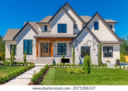 Large estate home with blue sky luxurious landscaping stone brick facade multiple peak roof and windows Royalty-Free Stock Photo #2071286537