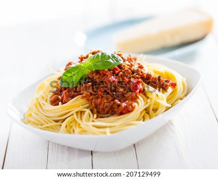 Healthy plate of Italian spaghetti topped with a tasty tomato and ground beef Bolognese sauce and fresh basil on a rustic white wooden table