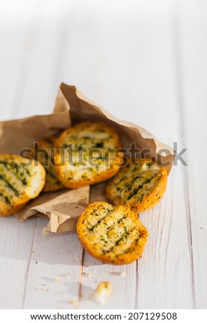 Golden crunchy grilled herb bread from the BBQ spilling from a torn brown paper packet on a rustic white wooden picnic table with copyspace
