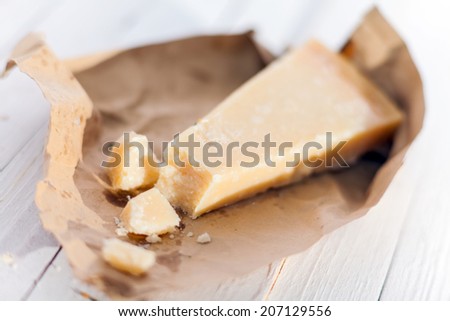 Wedge of fresh matured Italian Parmesan cheese or Parmigiano-Reggiano in a torn brown paper wrapper on white boards for use in Mediterranean cuisine