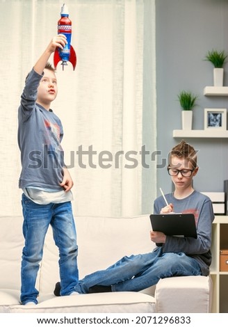 Two young brothers relaxing at home on the weekend, one standing on the sofa playing with a rocket as the older boys studies Royalty-Free Stock Photo #2071296833