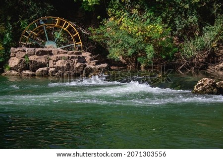 Greenish river flowing and hitting on rocks with old abandoned waterwheel built on rocks
