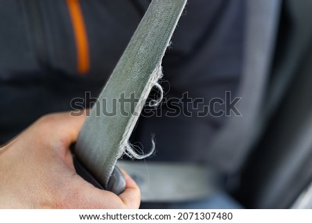 Macro closeup of man driver or passenger holding pulling old frayed ripped torn damaged car vehicle seat belt or seatbelt Royalty-Free Stock Photo #2071307480