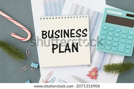 Business Plan text with a person holding a pen on a wooden desk
