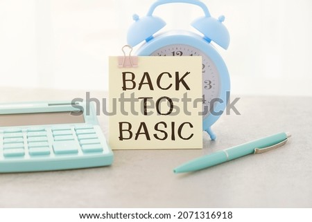 On the table are reports, a white alarm clock, a calculator, folders for papers, a pen and a white notebook with the text BACK TO BASICS. Business concept