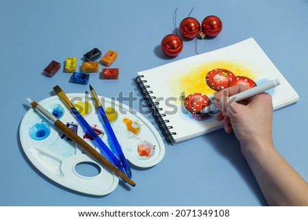 Christmas watercolor painting with artist's hand. Watercolor drawing of Christmas decorations. 