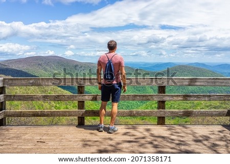 One young man with drawstring bag backpack standing on observation overlook deck wooden platform at Wintergreen ski resort town on nature Highlands leisure hiking trail, Virginia Royalty-Free Stock Photo #2071358171