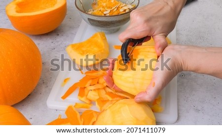 Woman hands peeling fresh raw orange pumpkin, close up on grey stone background