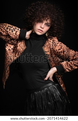 Fashionable portrait of a white Caucasian girl with African curls. Girl in a leopard-print jacket on a black background.