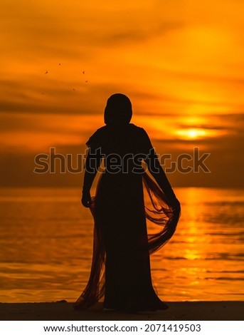 A vertical shot of a silhouette of a female in a dress on a beach at sunset