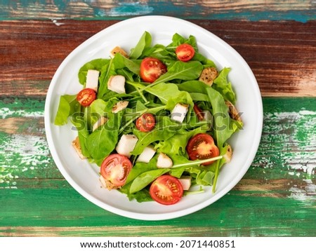 Fresh spinach salad with tomato, small pieces of herb roasted chicken in white ceramic dish on colourful wooded table. Concept for healthy. Studio picture.